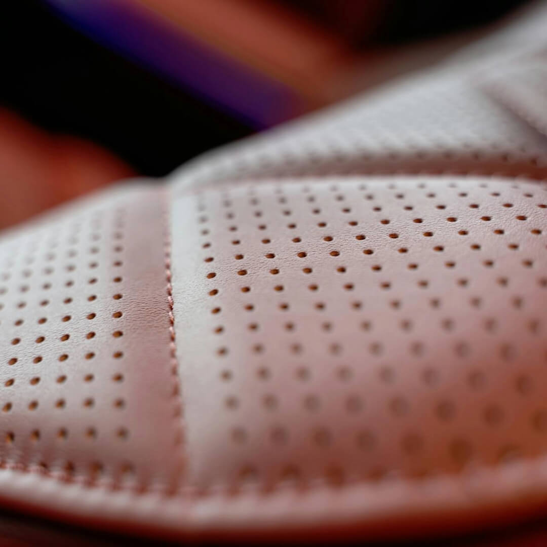 Close-up view of a perforated leather car seat cover, showing fine stitching and evenly spaced holes for enhanced breathability and comfort.