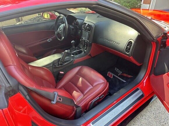 Interior view of a Corvette C6 featuring dark red faux leather seat covers with the Corvette logo prominently displayed on the headrests. The covers showcase a luxurious design with detailed stitching and ergonomic contours, providing a snug and stylish fit that enhances the car's interior aesthetic.