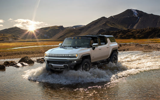 2024 GMC Hummer EV Pickup driving on an off-road trail, showcasing its robust design and powerful electric capabilities, symbolizing a new era for Hummer.