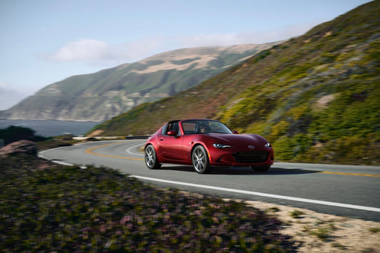 2024 Mazda MX-5 Miata RF on a curvy road, showcasing its sleek design and enhanced driving dynamics with updated features.