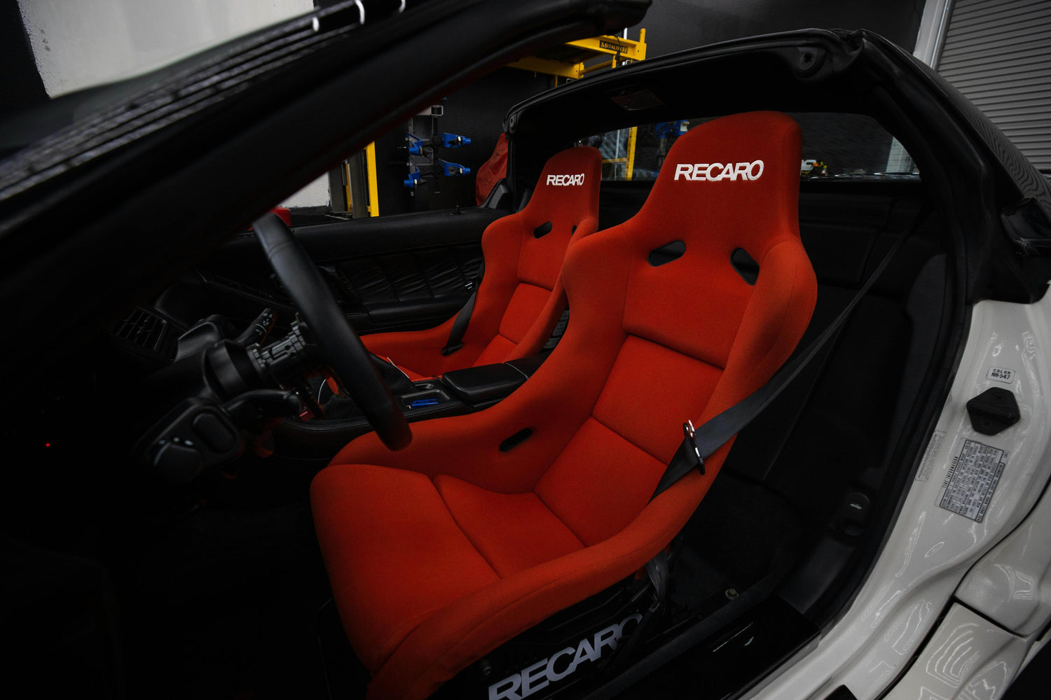 Interior view of a car featuring Recaro racing bucket seats in vibrant red, showcasing their ergonomic design and snug fit for high-performance driving.