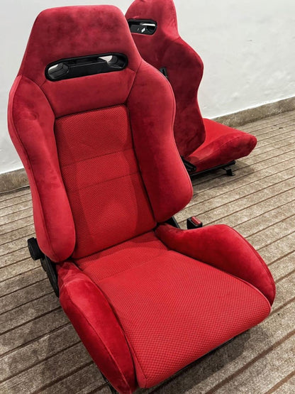 Side angle of a pair of Recaro SR3 Confetti DC2 Type R bucket seats in red suede, highlighting the reclining mechanism and sporty profile.